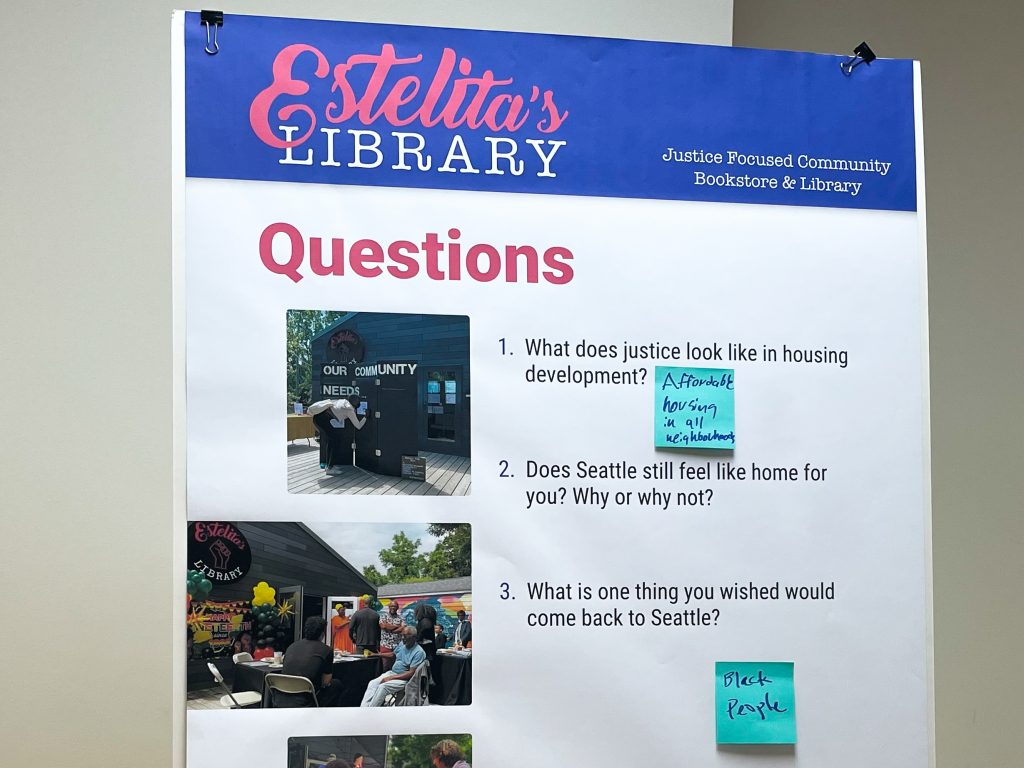 A photograph of a poster board at the Community Meeting. The poster shows several questions with blank spaces underneath them, and sticky notes showing people's answers to the questions stuck underneath.